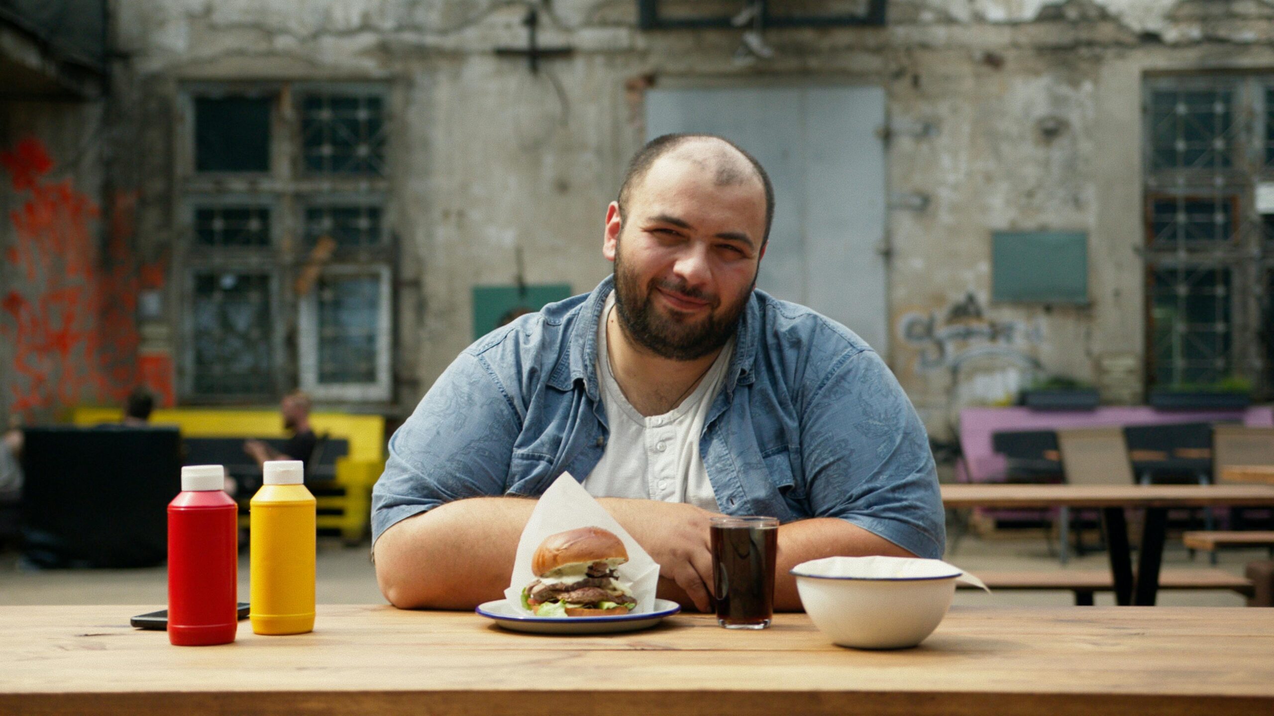 Smiling Man Sitting on a Wooden Table with Hamburger